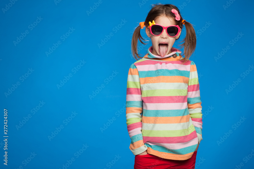 Portrait of an emotional girl of five years old in a striped sweater and in children's glasses on a blue background