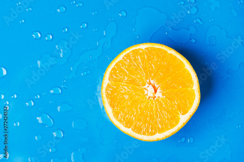 Raw juicy citrus fruit cut in half orange on wet blue background with water drops splashes. Summer beverages refreshments drinks cocktails juice ingredient. Healthy diet vitamins vegan concept