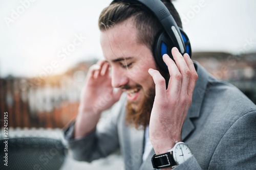 A young businessman with headphones on a terrace, listening to music.