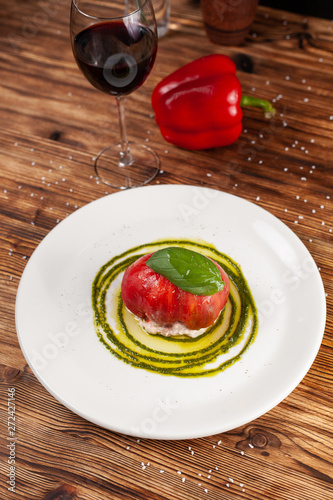Bull's Heart tomato, stuffed with tuna and cheese, flavoured with fresh pesto sauce and basil on a white plate