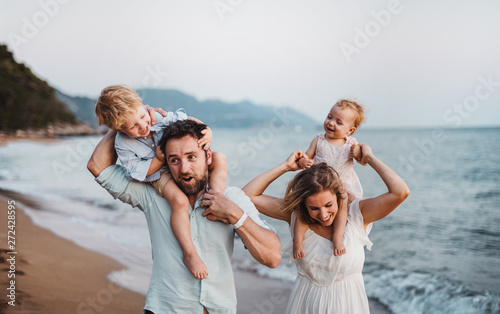 A young family with two toddler children standing on beach on summer holiday.