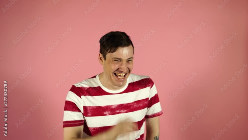 Young man in t-shirt laughing and smiling standing on pink background Young man in t-shirt laughing and smiling standing on pink background