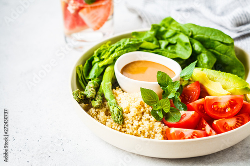 Green salad with quinoa, avocado and asparagus in a white bowl.