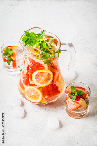 Grapefruit lemonade with lemon and mint in glass jug.