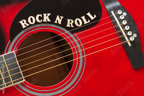 Words Rock N Roll with wooden letters, closeup on a surface of red acoustic guitar. Music entertainment background.