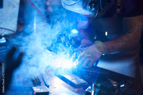 Close-up of busy welder in protective mask and gloves joining metal pieces with welding torch in workshop