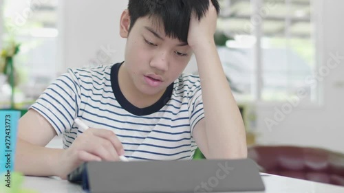 The bad-tempered Asian boy did his homework using a tablet computer to find information.  photo