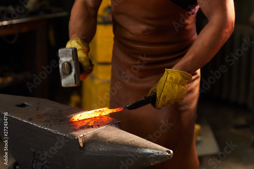 Photography Close-up of unrecognizable metalworker in leather apron and gloves standing by a