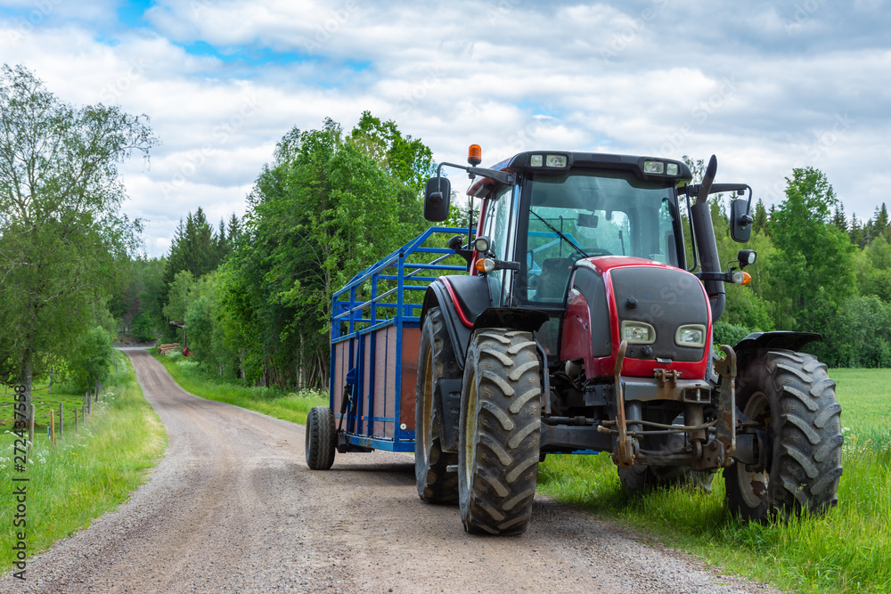 Tractor with trailer on the country side road with green trees and cloudy sky Tractor with trailer on the country side road with green trees and cloudy sky