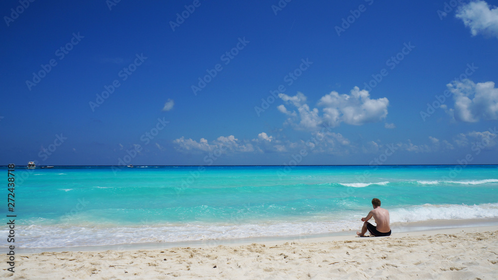 Man sitting on the Caribbean sea coast, Cancun sand beach, Mexico.