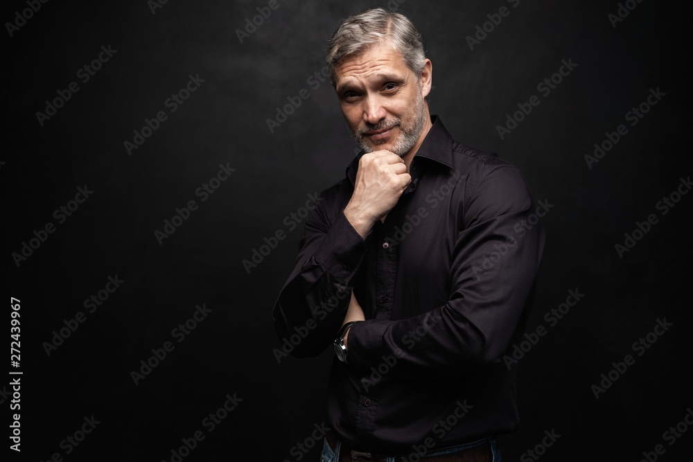 Fototapeta premium Middle-aged good looking man posing in front of a black background with copy space.