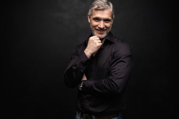 Middle-aged good looking man posing in front of a black background with copy space.