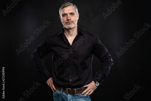 Middle-aged good looking man posing in front of a black background with copy space.