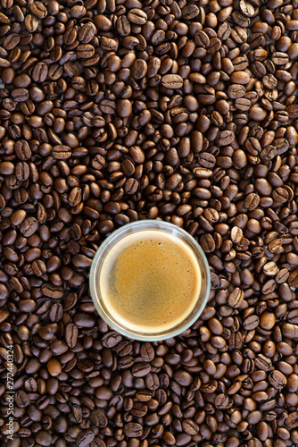 Espresso shot on a table filled with roasted coffee beans. High resolution