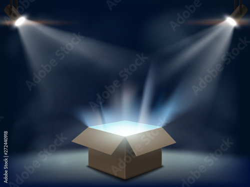 Open cardboard box with light inside. Background with spotlights