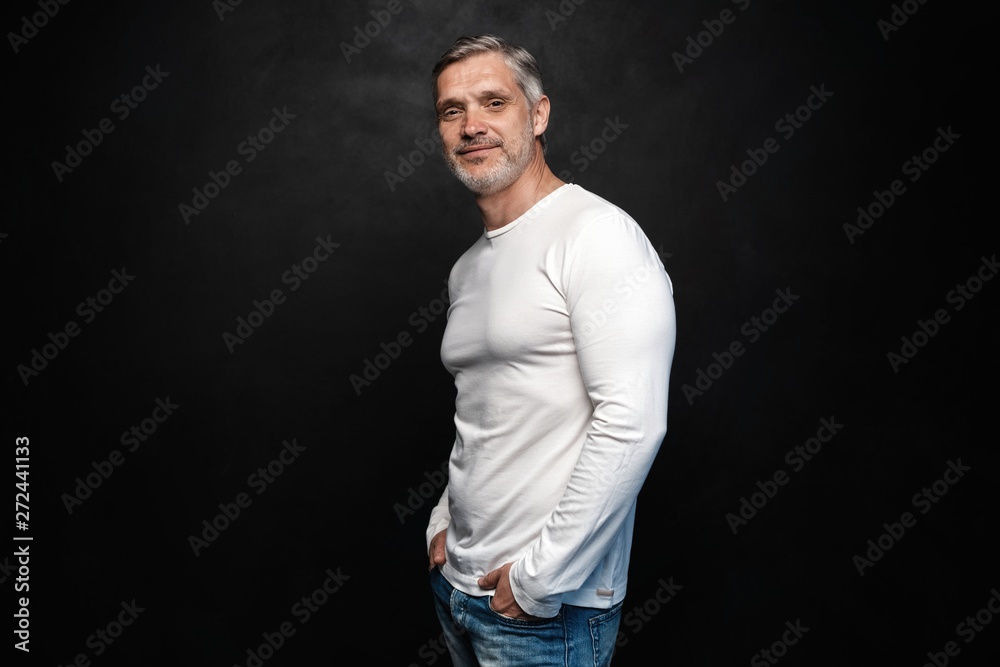 Middle-aged good looking man in white t-shirt posing in front of a black background with copy space. Middle-aged good looking man in white t-shirt posing in front of a black background with copy space.