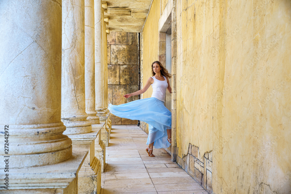 Young  woman in blue airy skirt in Ancient Greek ruins with old walls and columns
