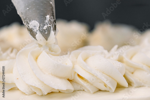 Decorating a white cake with cream from the pastry bag. Macro shot, closeup.