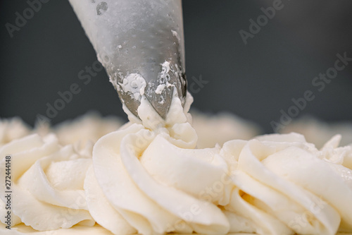 Decorating a white cake with cream from the pastry bag. Macro shot, closeup.