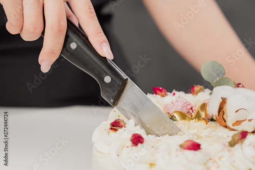 A condater cuts a beautiful fresh decorated white cake with a large knife.