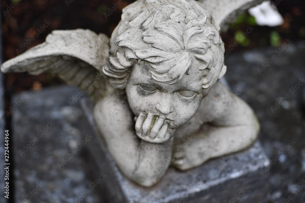 A white statue of a small angel on a christian cemetery in Berlin-Germany.