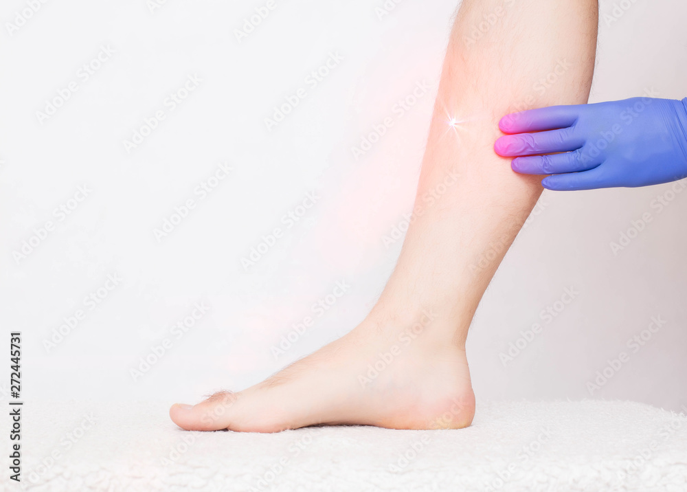 The doctor beautician conducts the procedure for a man laser hair removal of the leg, white background, copy space, hair removal The doctor beautician conducts the procedure for a man laser hair removal of the leg, white background, copy space, hair removal