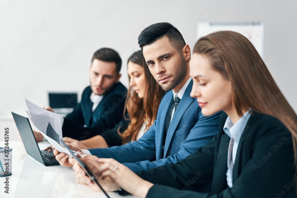 Portrait of smiling group of business people sitting in a row together at table in a modern office Portrait of smiling group of business people sitting in a row together at table in a modern office