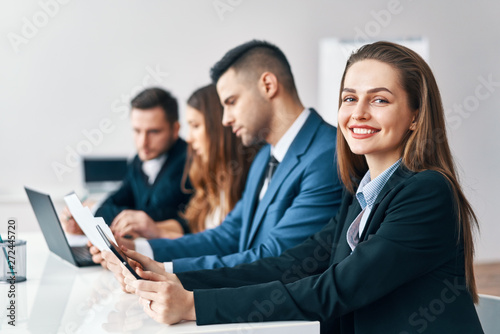 Portrait of smiling group of business people sitting in a row together at table in a modern office
