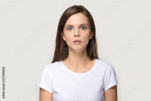 Scared girl looking at camera posing over grey studio background