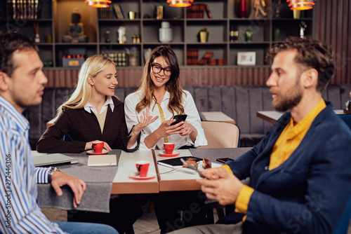 Multiethnic friends dressed sitting in cafe, drinking coffee , chatting and using smart phones.