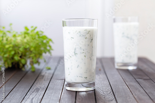 Fresh homemade yogurt (kefir, ayran) in glass with herbs. Ayran, homemade yogurt drink with herbs and cucumbers - healthy summer refreshing cold drink. Probiotic fermented dairy drink. Healthy food.  photo