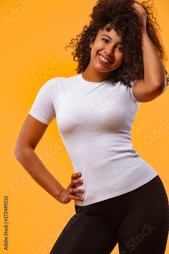 Smiling strong athletic woman with black skin and curly hair, doing exercise on yellow background wearing sportswear. Fitness and sport motivation. photo