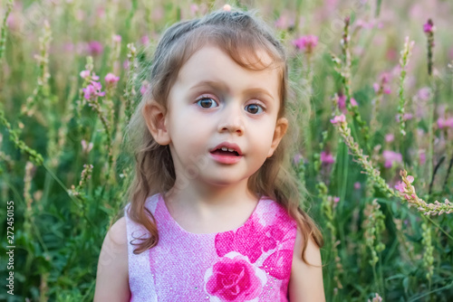 Cute surprised baby girl outdoors in green field. Child portrait