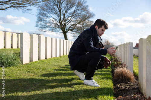 Man visiting grave at cemetery with phone in hand photo
