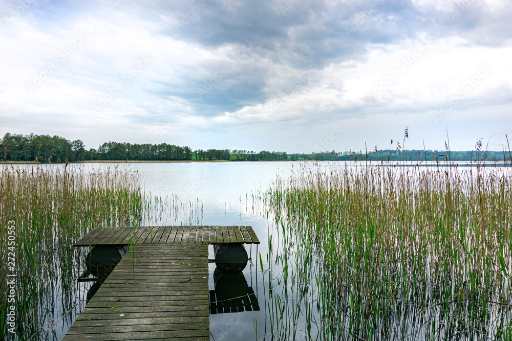 Obraz premium Beautiful view of the lake, wooden pier and water grass. Spring, Mazury, Poland.