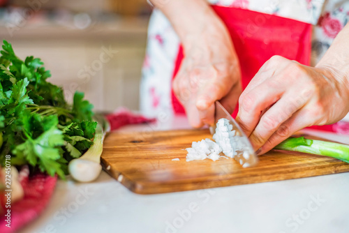 Female hand with knife cuts green leek in kitchen. Cooking vegetables