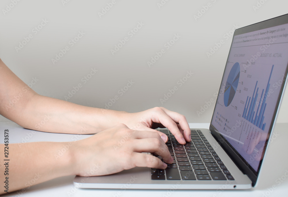 The side view of the businessman's hand is analyzing the graph using a laptop computer on a modern white desk. The side view of the businessman's hand is analyzing the graph using a laptop computer on a modern white desk.