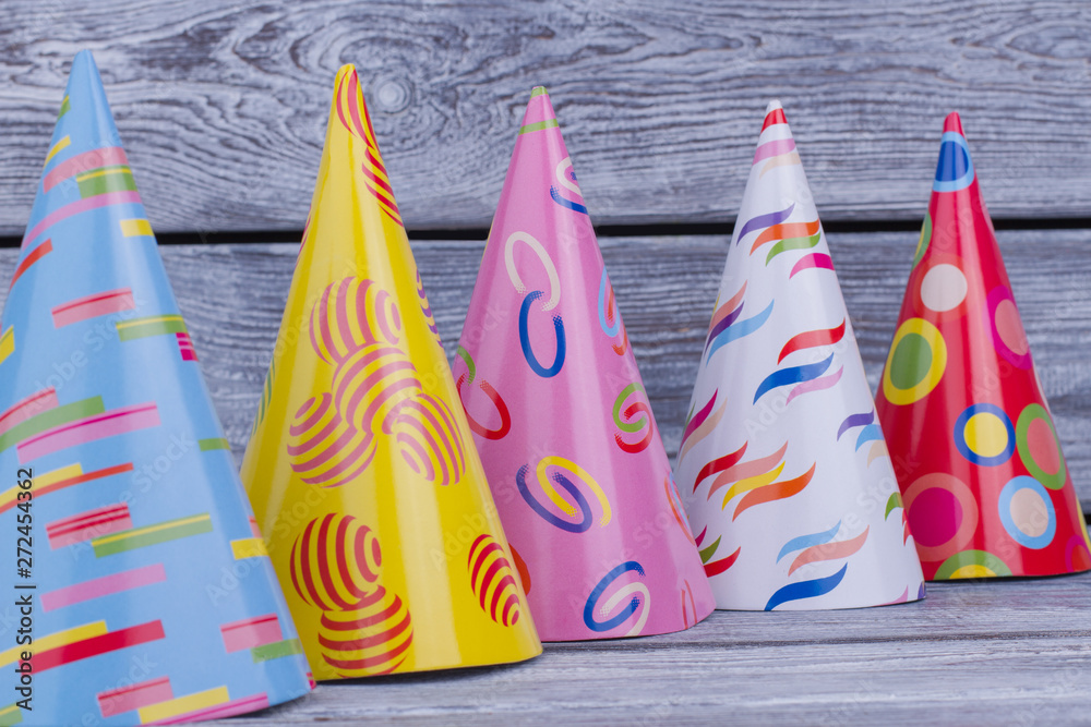 Assorted party hats on wooden background. Row of Birthday caps on wooden planks background. Birthday party supplies.