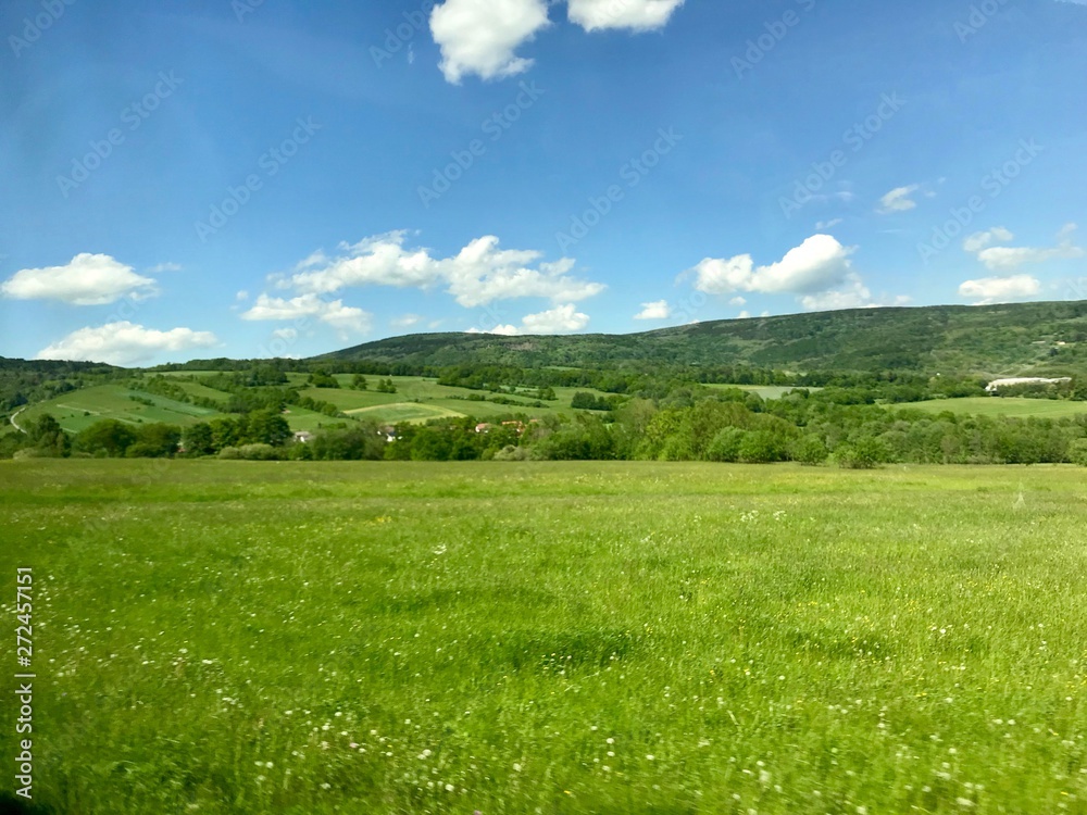 Scenic hike to the Kreuzberg (Calvary) in the Bavarian Rhoen region (Germany) on a beautiful sunny summer day through lush green landscape with grass, trees and a blue sky with white clouds