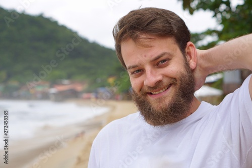 Close up portrait of a Brazilian man with blue eyes and a beard smiling on the beach