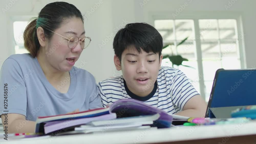 Mother helping her son to do his homework at home. Beautiful mother reading textbook and talking with son while doing homework together at home. Mother helping her son to do his homework at home. Beautiful mother reading textbook and talking with son while doing homework together at home.