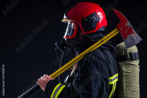 portrait strong fireman in fireproof uniform holding an ax in his hands black background studio © yurakrasil