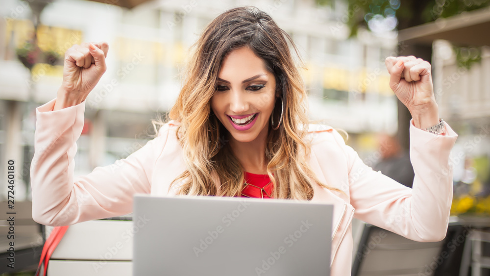 Woman sitting in cafe, front of laptop raising her hands