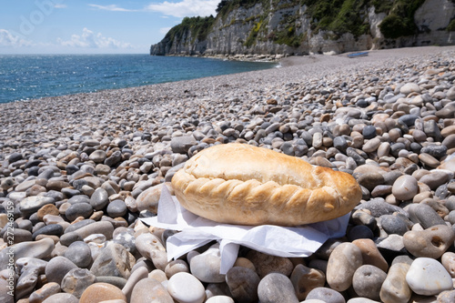 Canvas Print Cornish pasty on shingle beach with sea in background