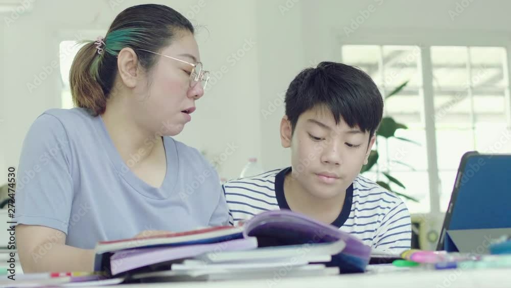 Mother helping her son to do his homework at home. Beautiful mother reading textbook and talking with son while doing homework together at home. Mother helping her son to do his homework at home. Beautiful mother reading textbook and talking with son while doing homework together at home.