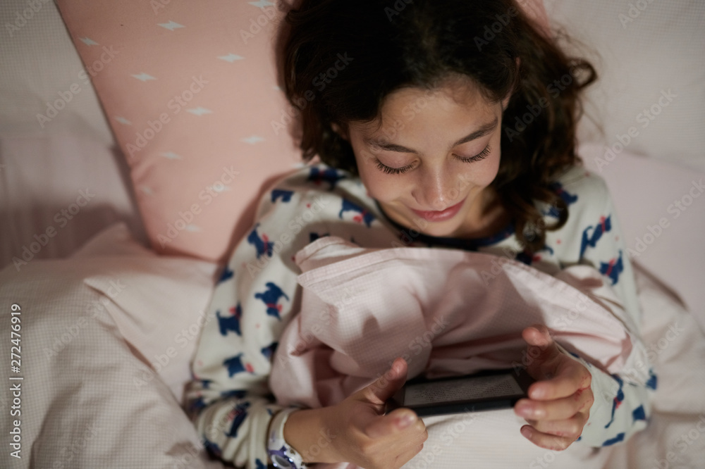 Smiling little girl reading ebook in her bed Smiling little girl reading ebook in her bed