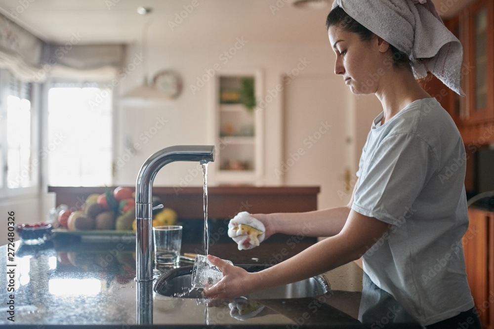 Woman with towel on head washing the glass in the kitchen. Woman with towel on head washing the glass in the kitchen.