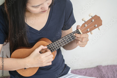 Closeup asian woman playing ukulele on white cement wall texture background with copy space