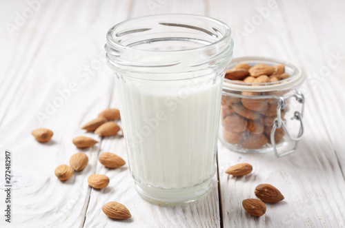 Milk or yogurt in mason jar on white wooden table with almonds in airtight conainer aside