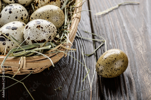 Fresh organic quail eggs in small wicker basket on rustic kitchen table. Space for text